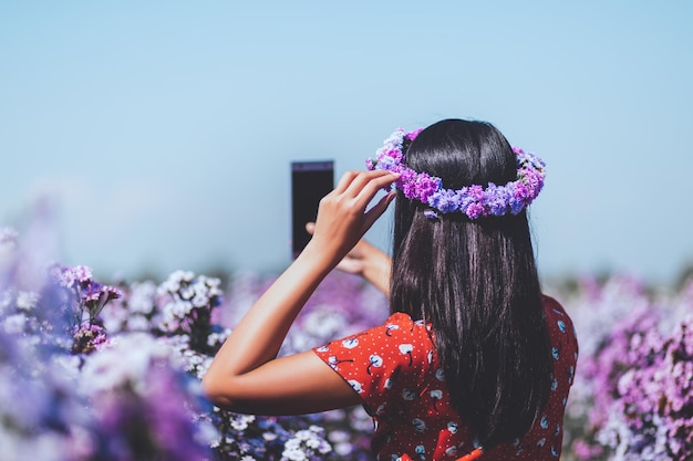 写真 花畑で携帯電話旅行を持つ旅行者の女性