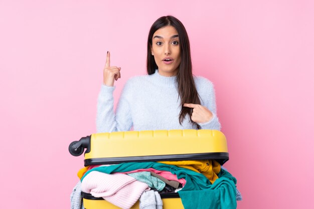 Donna viaggiatore con una valigia piena di vestiti su rosa con sorpresa espressione facciale