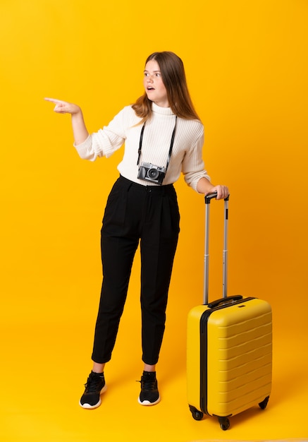 Traveler woman with a suitcase over isolated yellow background