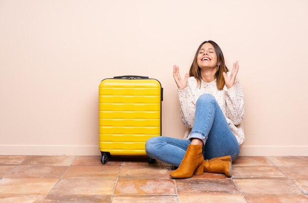 笑いながら床に座ってスーツケースを持つ旅行者女性