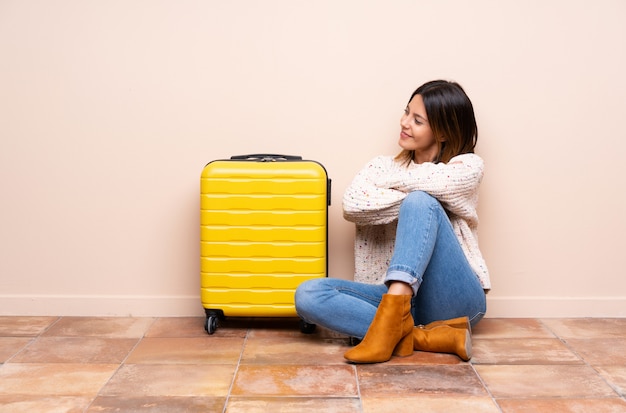 Traveler woman with suitcase sitting on the floor looking to the side