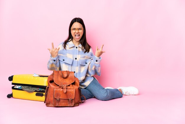 Traveler woman with a suitcase sitting on the floor making horn gesture