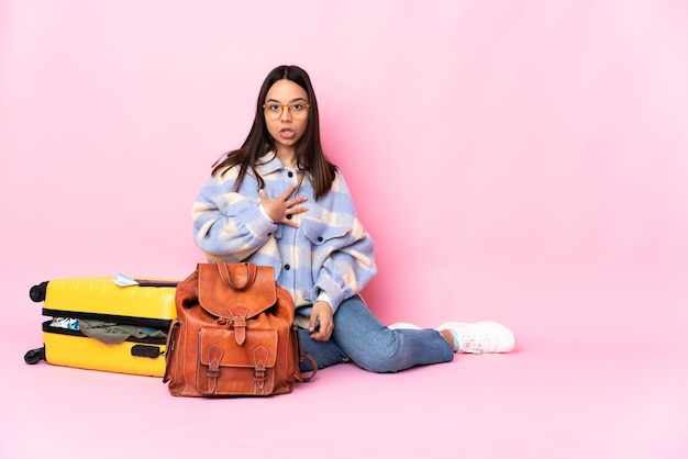 Traveler woman with a suitcase sitting on the floor surprised and shocked while looking right