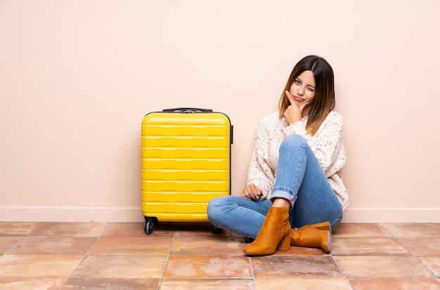 Traveler woman with suitcase sitting on the floor thinking an idea