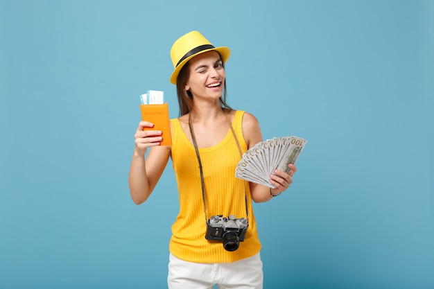 Donna viaggiatrice in abiti casual gialli e cappello che tiene la macchina fotografica dei soldi dei biglietti su blue