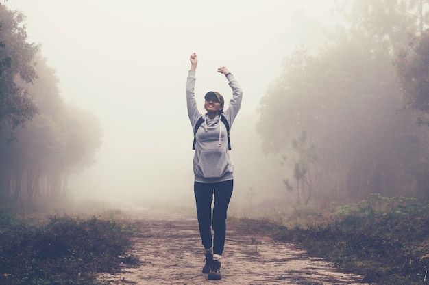 旅行者の女性は森と霧の中の森の道の道を歩いている