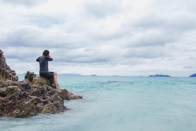 Photo traveler young woman sittng on stone coast and looking at the sea