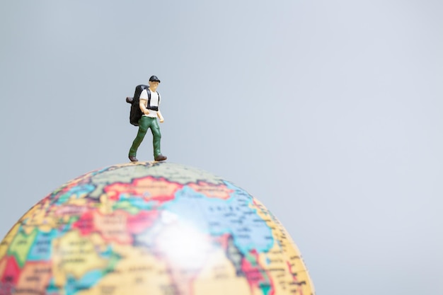 Travelers in miniature standing on the globe and making their way to their destination