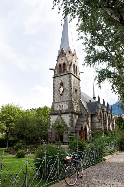 Travelers people stop bicycle and visit relax at garden of Chiesa evangelica di Cristo church at walkway riverside passer river in Meran city in Merano Italy