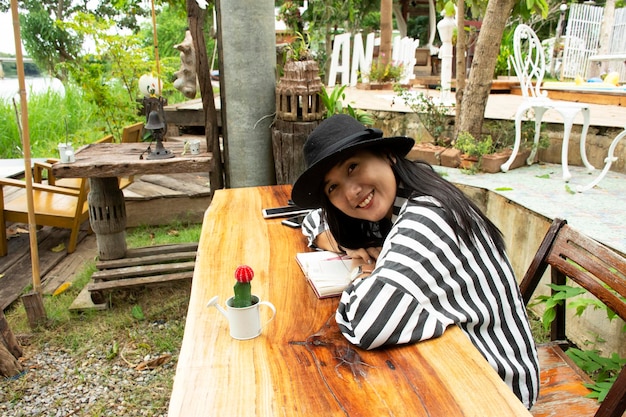 Travelers thai woman sit and writing note on the book for\
memory of detail between journey travel at ban pong in garden of\
resort in ratchaburi thailand