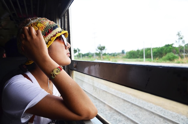 旅の探検家のために鉄道に座っている旅行者のタイの女性と窓の列車で写真を撮るためにポーズをとる肖像画は、目的地の旅行に行き、タイのバンコクからプラナコンシーアユタヤを訪れます