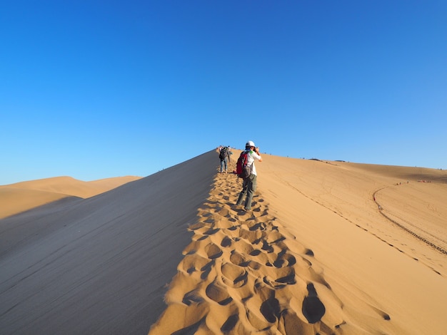 Photo travelers trekking to the top of desert mountain to see sunset in evening.