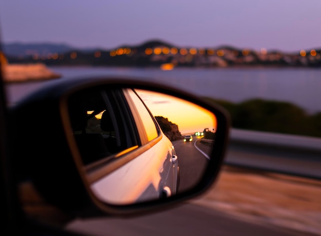 Traveling by car along beautiful coast at night Reflection of sunset at side mirror