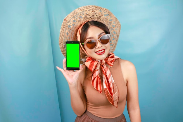Путешествующая концепция молодой азиатской счастливой женщины, показывающей пространство для копирования на своем смартфоне, изолированном синим фоном