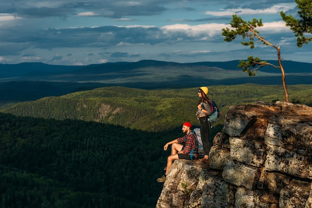 A traveling couple in hiking gear in the mountains at sunset. Two tourists on the top of the mountain. A man and a woman in the mountains. Hiking in the mountains with backpacks. Two travelers