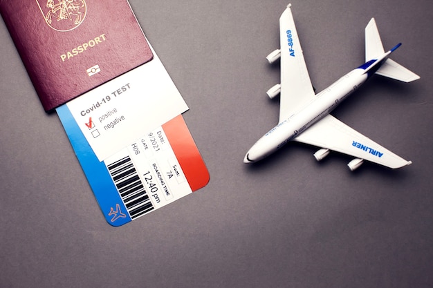 Photo traveling during covid-19 pandemic, passport with airline ticket, covid-19 positive test and plane on grey background, airport security health and safety check concept