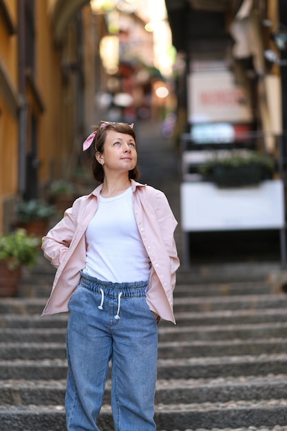 イタリアのかわいい通りや景色を楽しむブルージーンズピンクのシャツホワイトトップの旅行ファッションの女の子