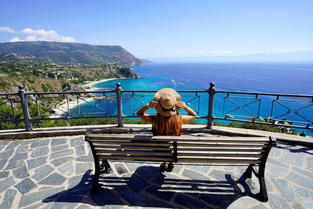 Traveling in Italy Panoramic view of fashion girl sitting on bench in Capo Vaticano viewpoint on the Coast of the Gods Calabria Italy
