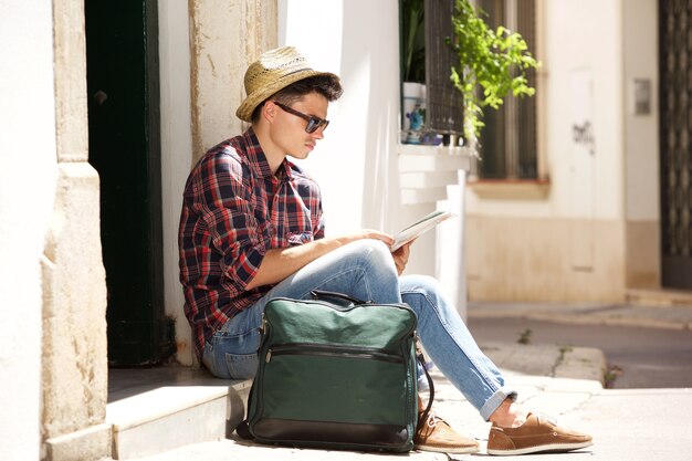 Traveling man sitting on sidewalk reading map