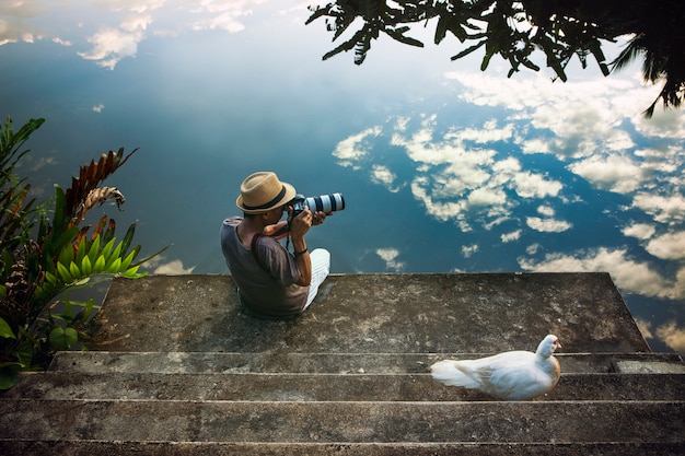 Traveling man taking a photograph at old pier against beautiful blue sky reflection on water floor