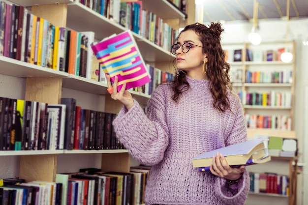 Traveling through library. serious concentrated girl carrying
opened book in raised hand while visiting book shop