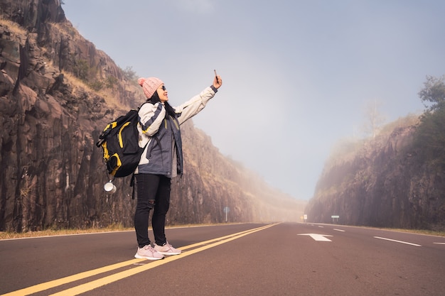 冬の山を背景にスマートフォンで自分の写真を撮る旅の女性。