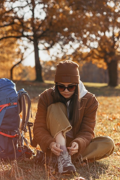 Traveling woman tying shoelaces on trekking boots during autumn hike in nature