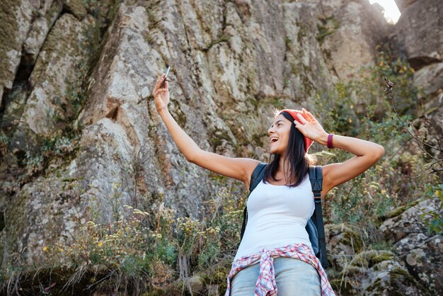 バックパックを持って旅行中の女性が岩の近くで自分撮りをします