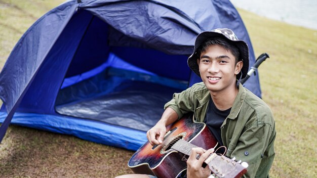 Uomo del viaggiatore a suonare la chitarra al campo