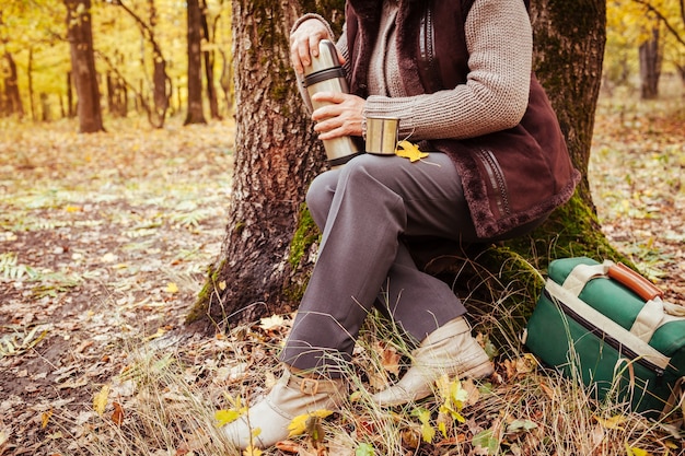 Traveller woman having rest and drinks tea in autumn forest