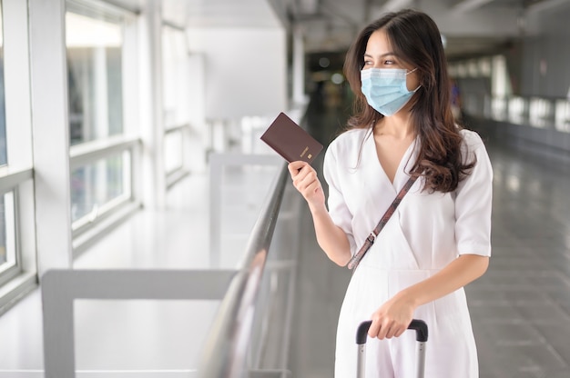 Una donna viaggiatrice indossa una maschera protettiva in aeroporto internazionale, viaggia sotto pandemia covid-19, viaggi di sicurezza, protocollo di allontanamento sociale, nuovo concetto di viaggio normale.