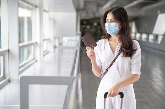 Una donna viaggiatrice indossa una maschera protettiva in aeroporto internazionale, viaggia sotto la pandemia covid-19,