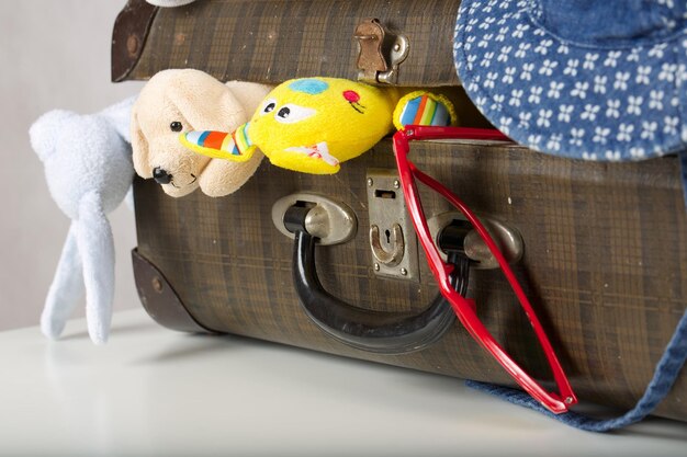 Travelling with children. Old-fashioned suitcase with items for children on a white table. White background