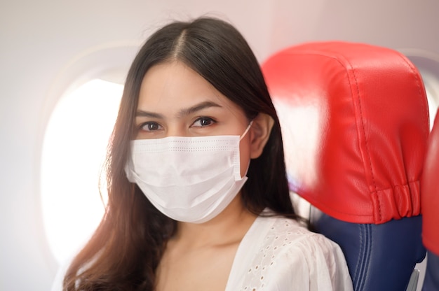 Una donna in viaggio indossa una maschera protettiva a bordo dell'aereo, viaggia sotto pandemia covid-19, viaggi sicuri, protocollo di allontanamento sociale