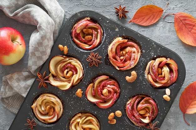 Tray of apple roses baked in puff pastry with autumn leaves and apples on dark