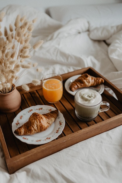 Photo a tray of breakfast on a bed with a glass of orange juice a cup of matcha latte and croissants