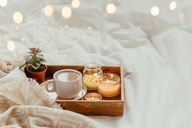 Tray of coffee and candles with warm plaid on white bedding . Breakfast in bed.    