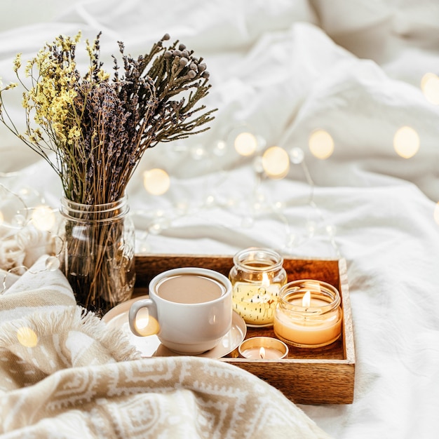 Tray of coffee and candles with warm plaid on white bedding . Breakfast in bed.    