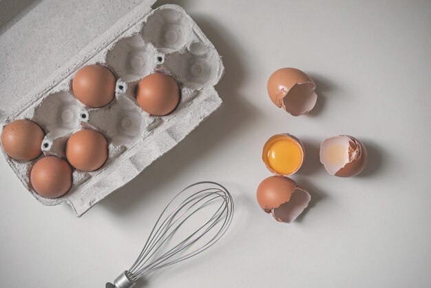 Tray of fresh raw eggs and broken egg shell on white background.