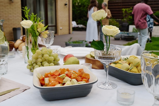 白いバラの花瓶の間に立つ、食欲をそそる野菜のシチュー、新鮮な果物、その他の夕食用の自家製料理が入ったトレイ