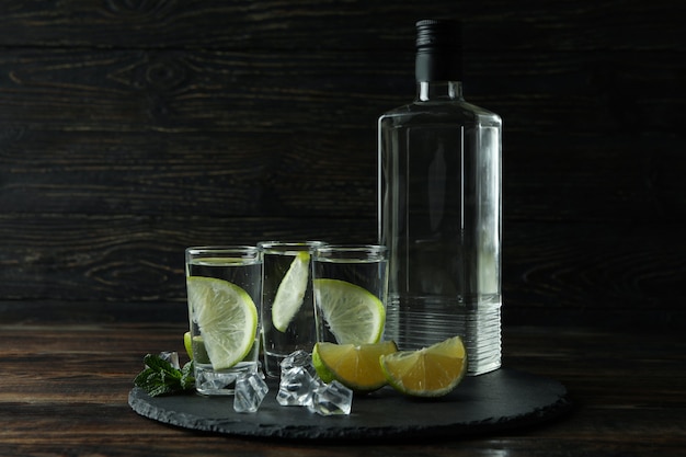 Tray with bottle and shots of vodka, lime and ice on wooden