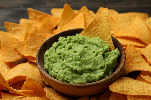 Tray with chips and bowl of guacamole on wooden background, close up