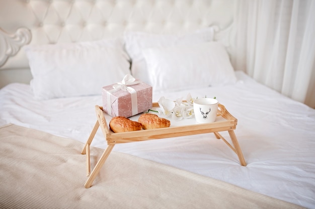 tray with coffee, croissants and a gift on bed