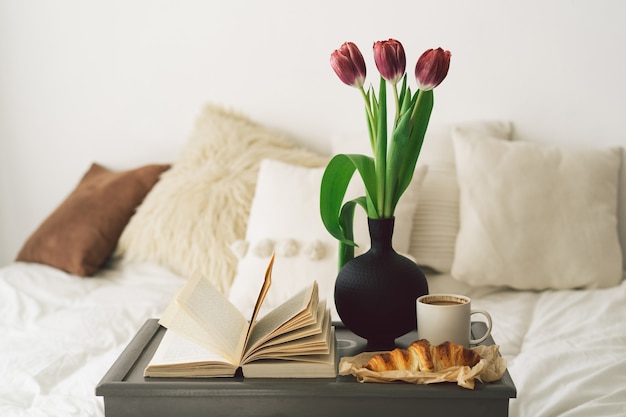 Vassoio con croissant, tazza di caffè e tulipano sul letto bianco pulito.