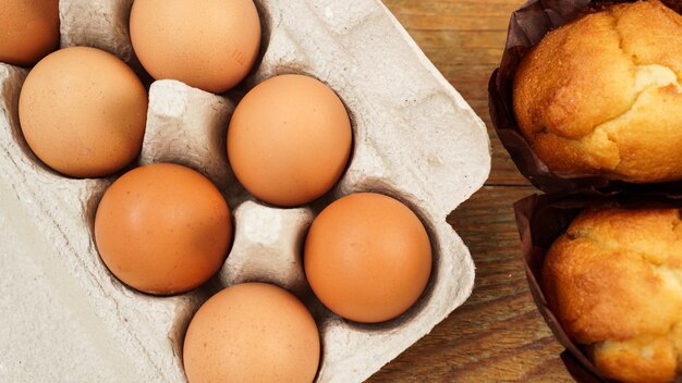 A tray with eggs and fresh tasty muffins in paper forms on a wooden background Horizontal photo