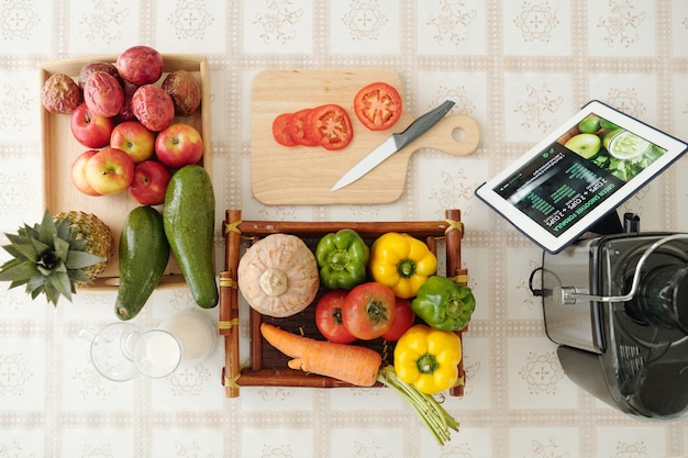 Tray with fresh vegetables, cutting board, knife and tablet computer with recipe on screen, viw from the top