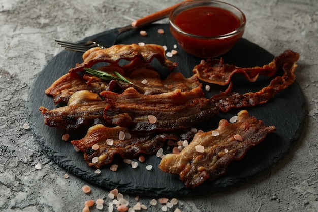 Tray with fried bacon on gray surface