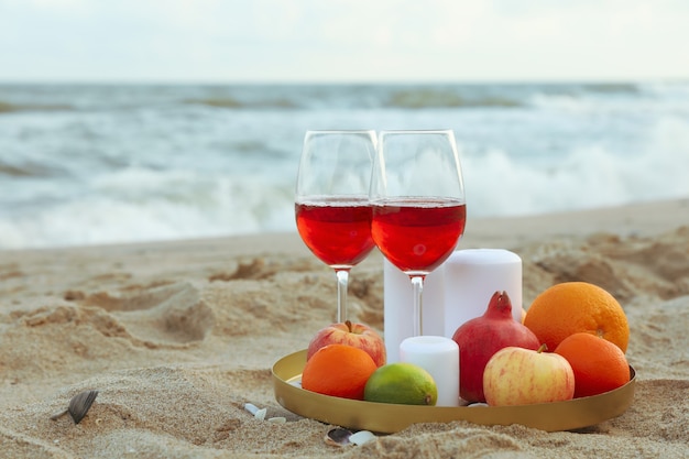 Photo tray with glasses of wine, fruits and candles on sandy sea beach