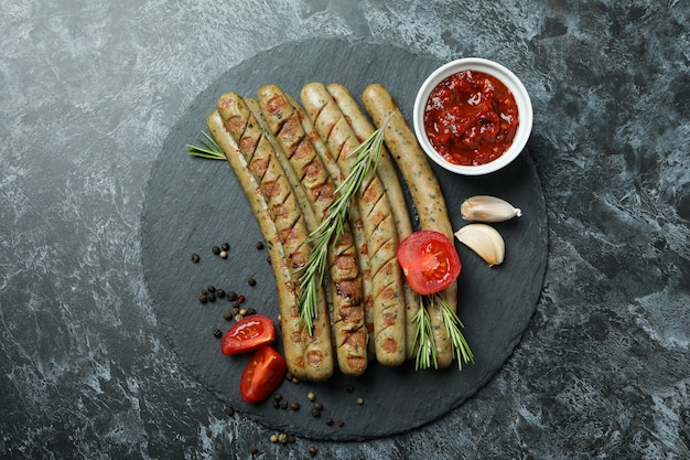 Tray with grilled sausage, spices and sauce on black smokey background