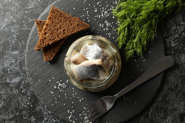 Tray with herring fish, salt, bread and dill on black smokey